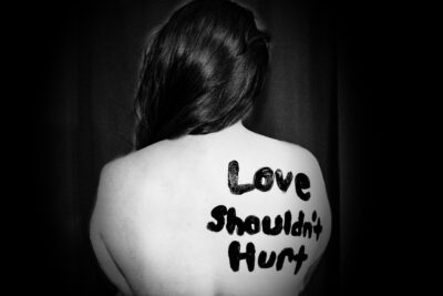 Mujer con mensaje en la espalda Love shouldn't hurt Conociendo las violencias Enlaza Consultoría de Género y Diversidad Photo by Sydney Sims on Unsplash